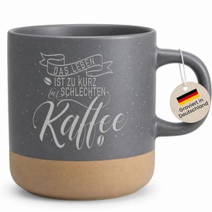 Könnte beinhalten: Graue Keramik-Kaffeetasse mit beigefarbenem Boden. Die Tasse hat weißen Text mit der Aufschrift "DAS LEBEN IST ZU KURZ für SCHLECHTEN Kaffee." Ein Anhänger mit der deutschen Flagge und dem Text "Graviert in Deutschland" hängt am Griff.