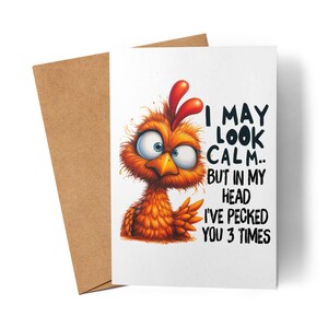 Peut inclure: Carte de vœux humoristique avec une illustration de poulet orange et une crête rouge. Le texte dit : « I MAY LOOK CALM.. BUT IN MY HEAD I'VE PECKED YOU 3 TIMES. » Une enveloppe marron est visible derrière la carte.