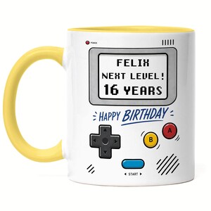 Könnte beinhalten: Weißer Keramikbecher mit gelbem Henkel und Innenraum. Der Becher hat ein Retro-Videospiel-Design mit dem Text "FELIX NEXT LEVEL! 16 YEARS" und "HAPPY BIRTHDAY".