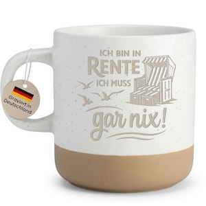 Könnte beinhalten: Weißer Keramikbecher mit beigefarbenem Boden und Henkel. Der Becher zeigt den deutschen Text "ICH BIN IN RENTE ICH MUSS gar nix!" zusammen mit einer Strandkorb-Grafik und fliegenden Vögeln. Ein Anhänger mit der deutschen Flagge ist angebracht.