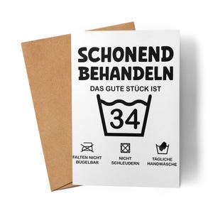 Könnte beinhalten: Eine weiße Grußkarte mit deutschem Text und Wäschezeichen, darunter "SCHONEND BEHANDELN" und "34" in einem Waschsymbol. Die Karte wird von einem braunen Umschlag begleitet.
