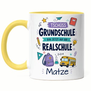 Könnte beinhalten: Eine weiße Keramiktasse mit gelbem Henkel und gelbem Innenraum, bedruckt mit bunten Schulmotiven und dem Text "TSCHÜSS GRUNDSCHULE BIN JETZT AUF DER REALSCHULE" sowie dem Namen "Matze" in dunkelblauer Schrift auf der Vorderseite.