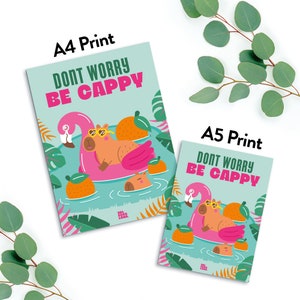 Puede incluir: Una impresi&oacute;n azul claro y verde con un capibara con gafas de sol flotando en un flotador de piscina rosa en forma de flamenco. El texto "Don't Worry Be Cappy" est&aacute; escrito en letras negras. La impresi&oacute;n est&aacute; disponible en tama&ntilde;os A4 y A5.