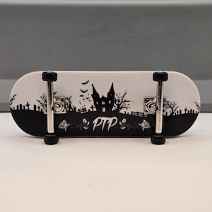 以下が含まれることがあります： 黒と白のフィンガーボードで、幽霊屋敷のグラフィックと下部に「PTP」の文字が書かれています。フィンガーボードには黒い車輪と銀色のトラックが付いています。