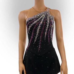 Puede incluir: Vestido negro de patinaje artístico con diseño asimétrico. El corpiño está adornado con un patrón de cristales rosas y transparentes. La falda es negra y tiene forma de línea A. El vestido tiene un panel de malla color nude en el hombro.