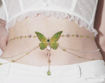 Puede incluir: Una cadena de cuerpo de oro con un dije de mariposa verde y detalles de gemas verdes.