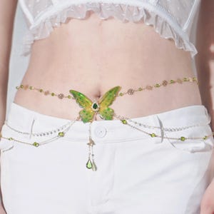 K&ouml;nnte beinhalten: Ein goldener Ketten-K&ouml;rper-Schmuck mit einem gr&uuml;nen Schmetterlings-Anh&auml;nger und gr&uuml;nen Kristall-Akzenten.