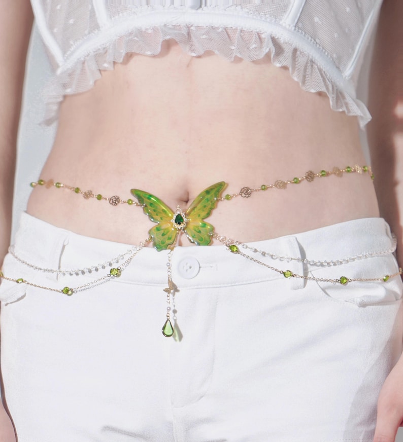 K&ouml;nnte beinhalten: Ein goldener Ketten-K&ouml;rper-Schmuck mit einem gr&uuml;nen Schmetterlings-Anh&auml;nger und gr&uuml;nen Kristall-Akzenten.