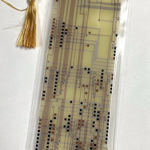 May include: A rectangular bookmark with a circuit board pattern in beige, brown, and black, protected by clear plastic. A gold tassel hangs from the top. Ideal for book enthusiasts, this bookmark is a unique accessory.