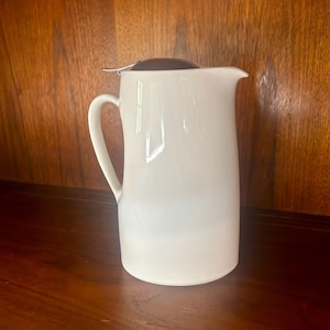 May include: White ceramic teapot with a stainless steel lid and a strainer. The teapot has a rounded body and a handle.