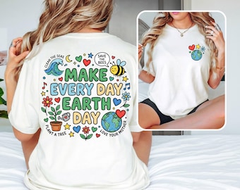 May include: Cream-colored t-shirt with a colorful graphic promoting environmental awareness. The design includes the text "MAKE EVERY DAY EARTH DAY" with illustrations of a wave, bee, flowers, and a globe. The shirt also features the phrases "CLEAN THE SEAS", "SAVE THE BEES", "PLANT A TREE", and "LOVE YOUR MOTHER".