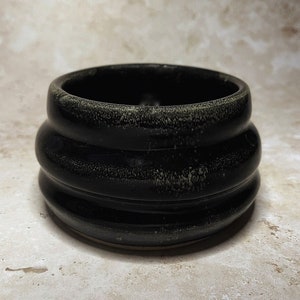 Puede incluir: Un cuenco de cerámica negro con un diseño texturizado y ondulado. El cuenco tiene un tono ligeramente verde y un acabado brillante.