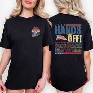 Può includere: Una maglietta nera con una grafica in stile vintage della Statua della Libertà e il testo "Hands Off!" sul davanti. La parte posteriore della maglietta presenta una bandiera americana in stile vintage con il testo "Hands Off!" e un elenco di elementi tra cui "Medicaid, Medicare, Sicurezza sociale, I nostri lavori, I nostri portafogli, I nostri libri, Elezioni eque, Dati personali, Terre pubbliche, Servizi per i veterani, Ricerca sul cancro, NATO, Protezioni dei consumatori, Aria pulita, Energia pulita, Scuole, Biblioteche, Libertà di parola, Diritti LGBTQ, Immigrati, Tribunali, Immigrati."