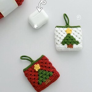 May include: Crocheted AirPod cases in red and white, each featuring a green Christmas tree design with a yellow star. The cases have a loop for hanging. A white AirPod case is also shown. Red yarn is visible in the background.