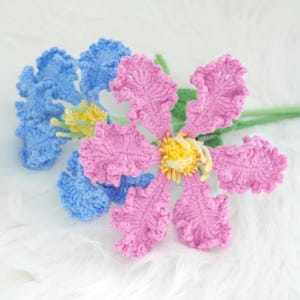 May include: Two crocheted flowers, one pink and one blue, with green stems. The flowers have a detailed, textured design.