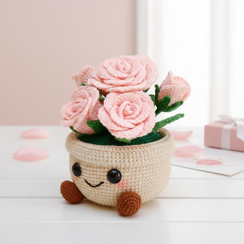 May include: A crocheted flower pot with a smiling face, holding pink roses and green leaves. The pot is beige with brown feet and black eyes. A charming handmade floral decoration.