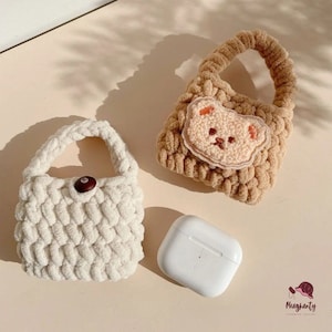 以下が含まれることがあります： 2つの小さなかぎ針編みのハンドバッグ。1つは白で茶色のボタンが付いており、もう1つは茶色で茶色のクマの顔のアップリケが付いています。白いAirPodケースも画像に写っています。