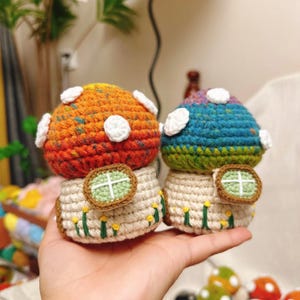 May include: Two crocheted mushroom houses with colorful tops and white accents. The houses have small windows and are decorated with green grass and yellow flowers.