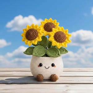 Pode incluir: Um arranjo de girassóis de crochê em um vaso branco com um rosto sorridente e pequenos pés marrons. Os girassóis têm pétalas amarelas e centros marrons, com folhas verdes. O fundo é um céu azul com nuvens brancas.