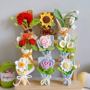May include: A collection of nine small, handcrafted crochet flower bouquets arranged on a wooden stand. Each bouquet features different flowers including sunflowers, roses, lilies, and daisies in vibrant colours like red, yellow, pink, and white.