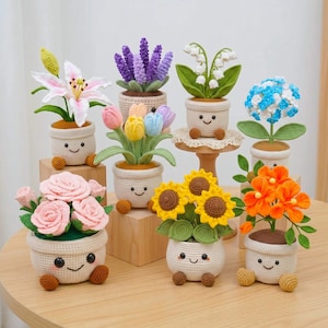 May include: A collection of eight crocheted potted plants, each featuring a beige pot with a smiling face and small brown feet. The plants include pink roses, a white lily, purple lavender, white lily of the valley, tulips, sunflowers, and orange flowers.