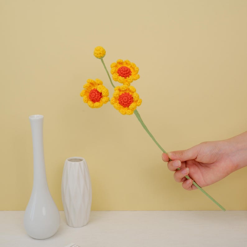 May include: A bouquet of crocheted yellow and orange flowers with green stems in a hand.
