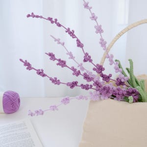 Puede incluir: Un ramo de flores de lavanda de ganchillo de color púrpura en una cesta tejida. Las flores están dispuestas en un jarrón y son una hermosa adición a cualquier decoración del hogar.