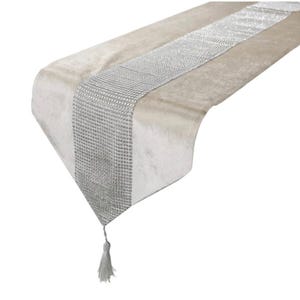 May include: A beige velvet table runner with a silver, textured central stripe. The runner has a tassel at the end. This decorative piece adds elegance to any dining table or event.