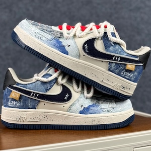 May include: Two pairs of blue and white sneakers with denim-like fabric. The shoes have a white swoosh, red laces, and the word "Love" printed on the side. The shoes are stacked on top of each other.