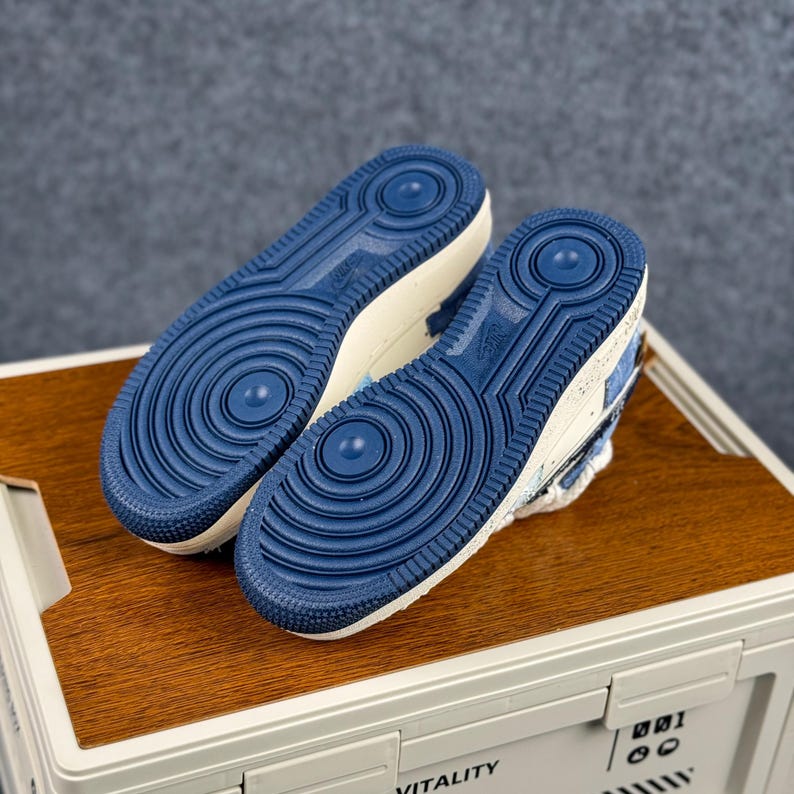 May include: Pair of blue and white sneakers with a textured design. The soles are a solid blue with a circular pattern. The shoes are placed on a wooden surface.