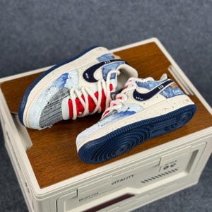 May include: A pair of white and blue sneakers with a navy blue swoosh logo. The sneakers feature red and white laces, and the words "MANIC" and "Love" are visible on the sides. The soles are navy blue.