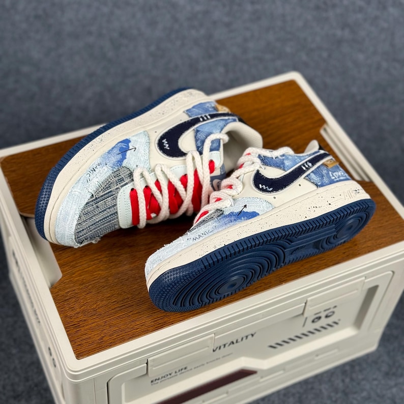 May include: A pair of white and blue sneakers with a navy blue swoosh logo. The sneakers feature red and white laces, and the words "MANIC" and "Love" are visible on the sides. The soles are navy blue.