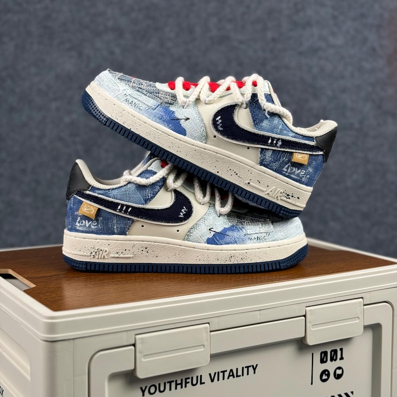 May include: Two pairs of blue and white sneakers with denim-like fabric. The shoes have a white swoosh, red laces, and the word "Love" printed on the side. The shoes are stacked on top of each other.