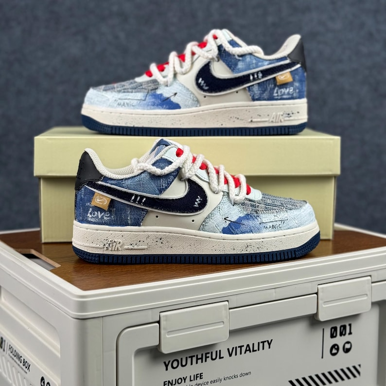 May include: Pair of blue and white sneakers with red laces. The shoes feature a denim-like pattern with navy blue accents, a white swoosh, and the word "Love" on the side. The soles are white with a navy blue trim.