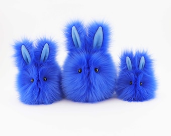 May include: Three blue plush bunny toys of different sizes, with light blue ears and black eyes. The bunnies are arranged in a row from largest to smallest.