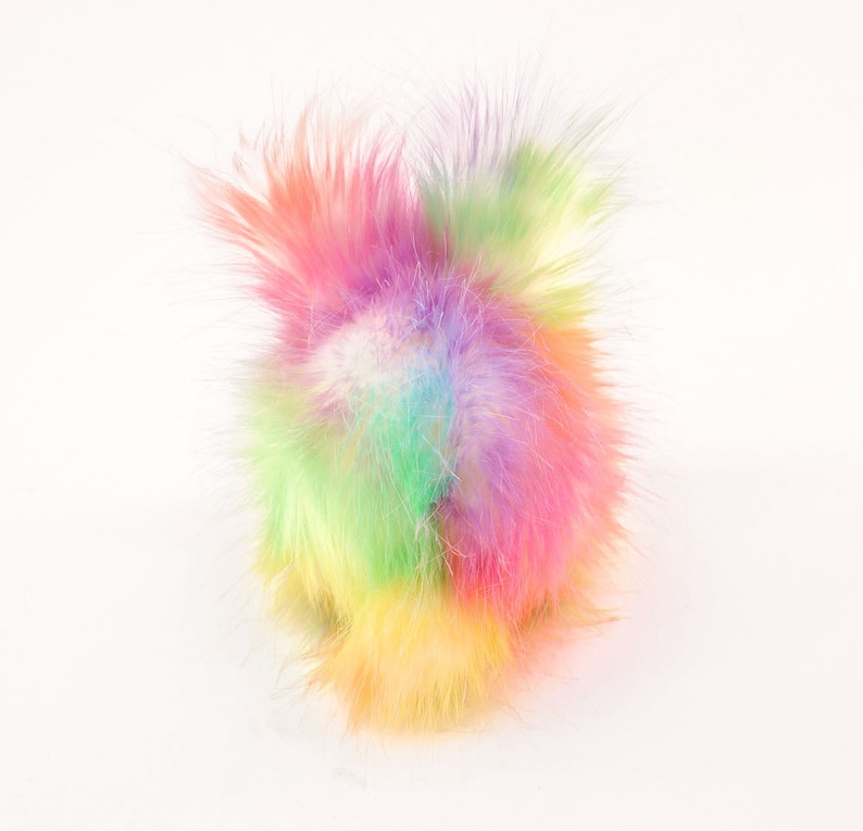 May include: A fluffy rainbow pom pom made of soft, colourful fur. The pom pom is a vibrant mix of pink, purple, green, yellow, and blue.