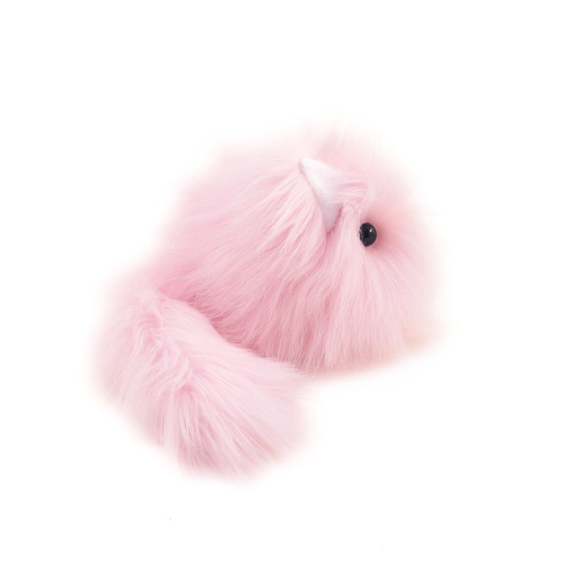 May include: A pink fluffy toy with a long tail and a small black eye. The toy is made of soft, plush material and has a white horn on its head.