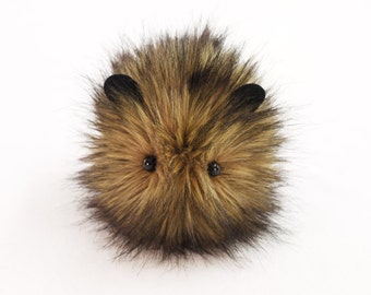 May include: A brown and black fluffy plush toy with black button eyes. The toy is shaped like a small animal with a round body and short, pointed ears.