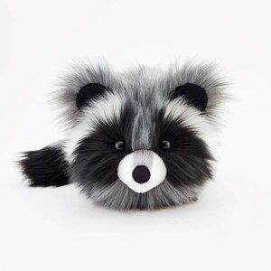 Pu&ograve; includere: Un giocattolo di peluche di procione con pelliccia bianca e nera. Il procione ha il naso nero e gli occhi neri. Il giocattolo &egrave; seduto su uno sfondo bianco.