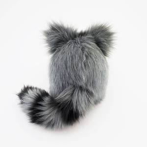Pu&ograve; includere: Un cappello di pelliccia sintetica grigio e nero con una lunga coda. Il cappello ha due grandi orecchie soffici.
