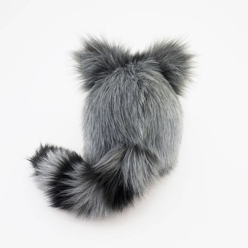 Pu&ograve; includere: Un cappello di pelliccia sintetica grigio e nero con una lunga coda. Il cappello ha due grandi orecchie soffici.
