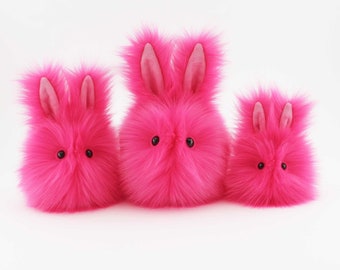 May include: Three pink fluffy bunny plushies of different sizes. The bunnies have black eyes and pink ears.