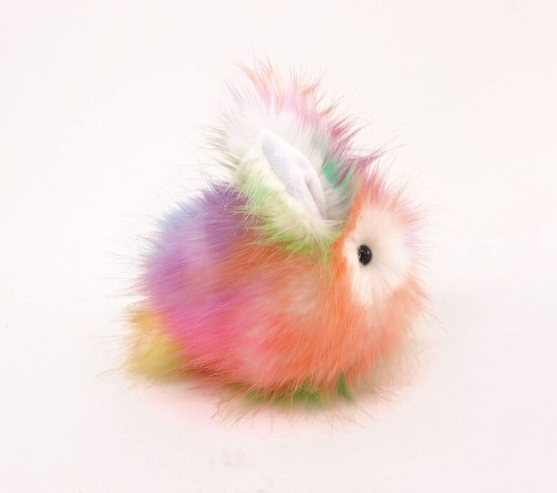 May include: A fluffy rainbow-coloured plush bunny toy with white ears and black eyes.