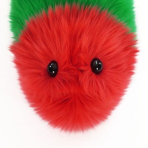 May include: A red fuzzy toy with two black eyes. The toy is made of soft, plush material and has a round shape.