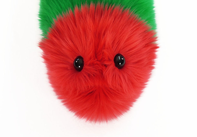 May include: A red fuzzy toy with two black eyes. The toy is made of soft, plush material and has a round shape.