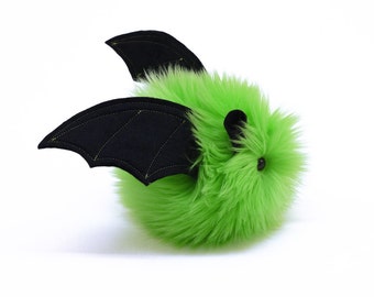 May include: A fluffy, lime green bat toy with black wings and small black ears. The wings are stitched with yellow thread. The toy is made of soft material and has a small, round black eye.
