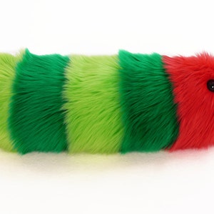 May include: A plush toy shaped like a caterpillar with green, lime green, and red stripes. The caterpillar has a black button eye.
