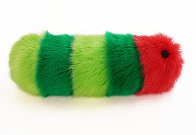 May include: A plush toy shaped like a caterpillar with green, lime green, and red stripes. The caterpillar has a black button eye.
