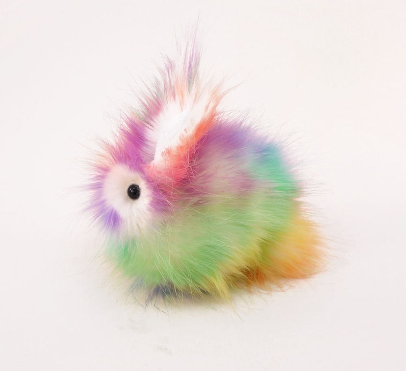 May include: A fluffy rainbow-coloured plush bunny toy with a white ear and a black eye.