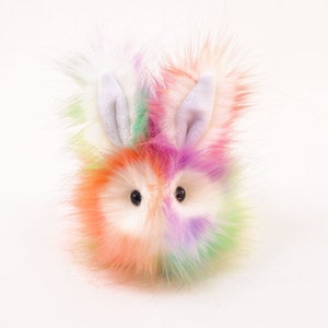 May include: A colourful fluffy toy bunny with white ears and black eyes. The bunny is made of soft, plush fabric and has a rainbow-coloured fur.